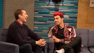 Joe Jonas Wears a Maroon and Gold Letterman Jacket With White Sneakers